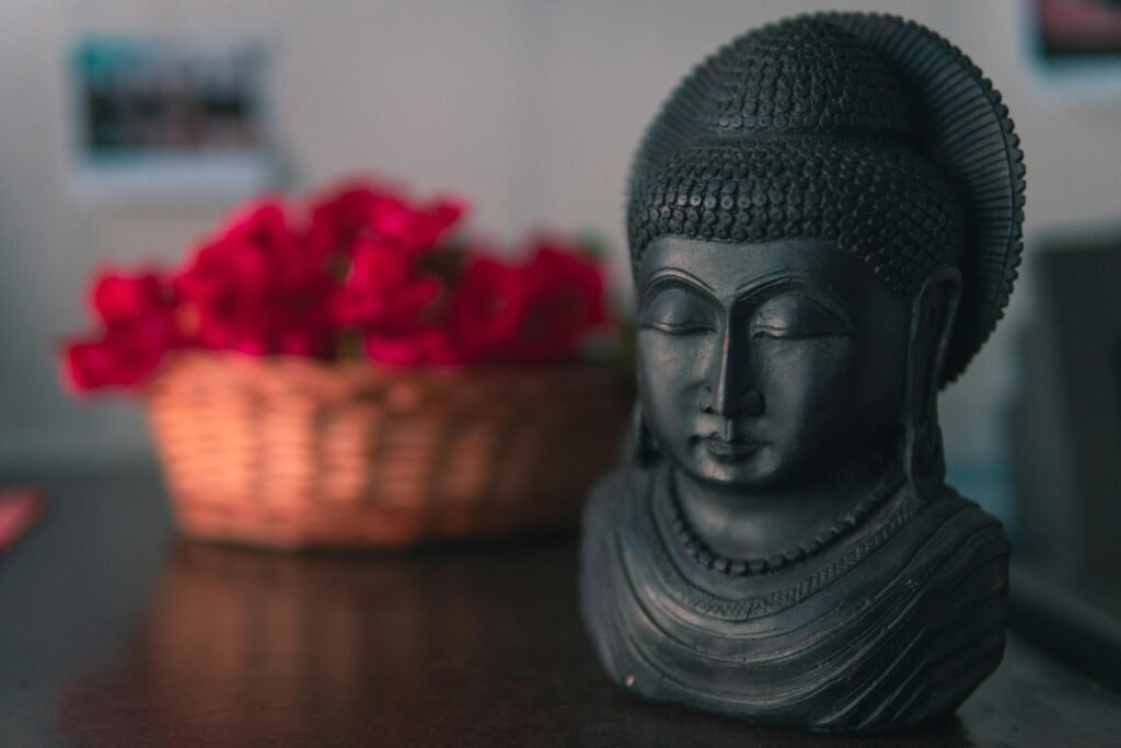 A dark Buddha sculpture indoors with a basket full of vibrant red flowers.