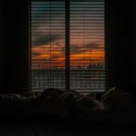 Cozy bedroom with a view of a vibrant sunset through window blinds.